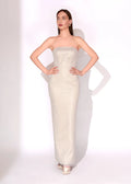 A woman modeling a strapless, floor-length champagne-colored sequined gown against a white studio background.